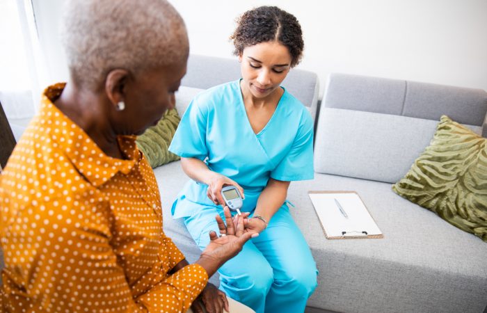 Young nurse doing a glucose blood test on her senior patient, during a home visit