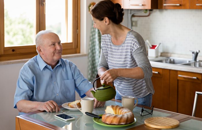 Female caregiver helping senior man, kitchen